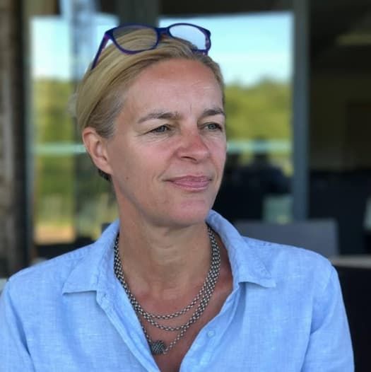 Portrait de Christine den Boer en chemise bleu clair, lunettes relevées sur la tête